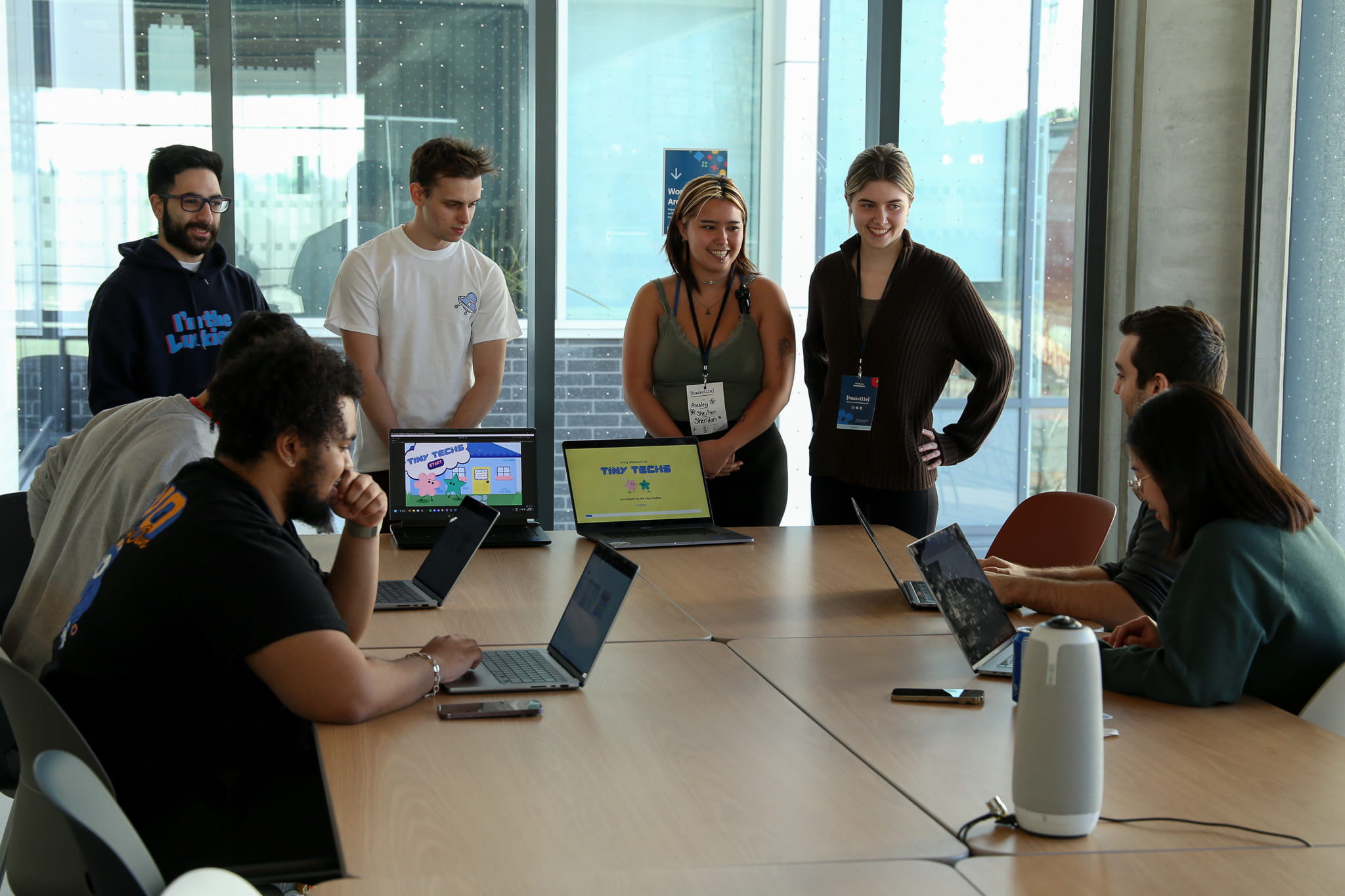 A group of students gather around a table as they look at a presentation on a laptop